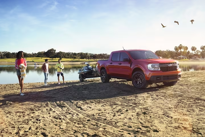 a red 2023 ford maverick parked on a sandy beach next to a body of water