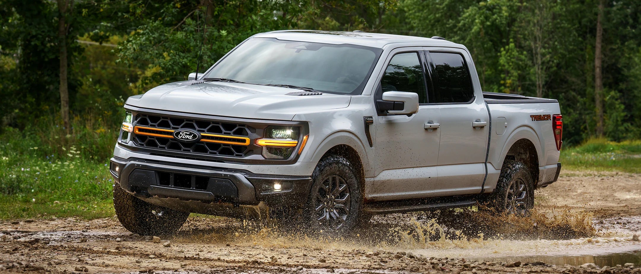 a silver 2025 ford f-150 tremor driving through muddy water and dirt roads.