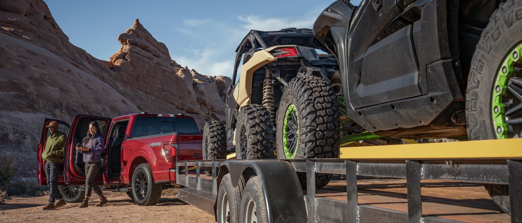 a red 2025 ford f-150 hauling a trailer with utvs on the back in the mountain area of a desert
