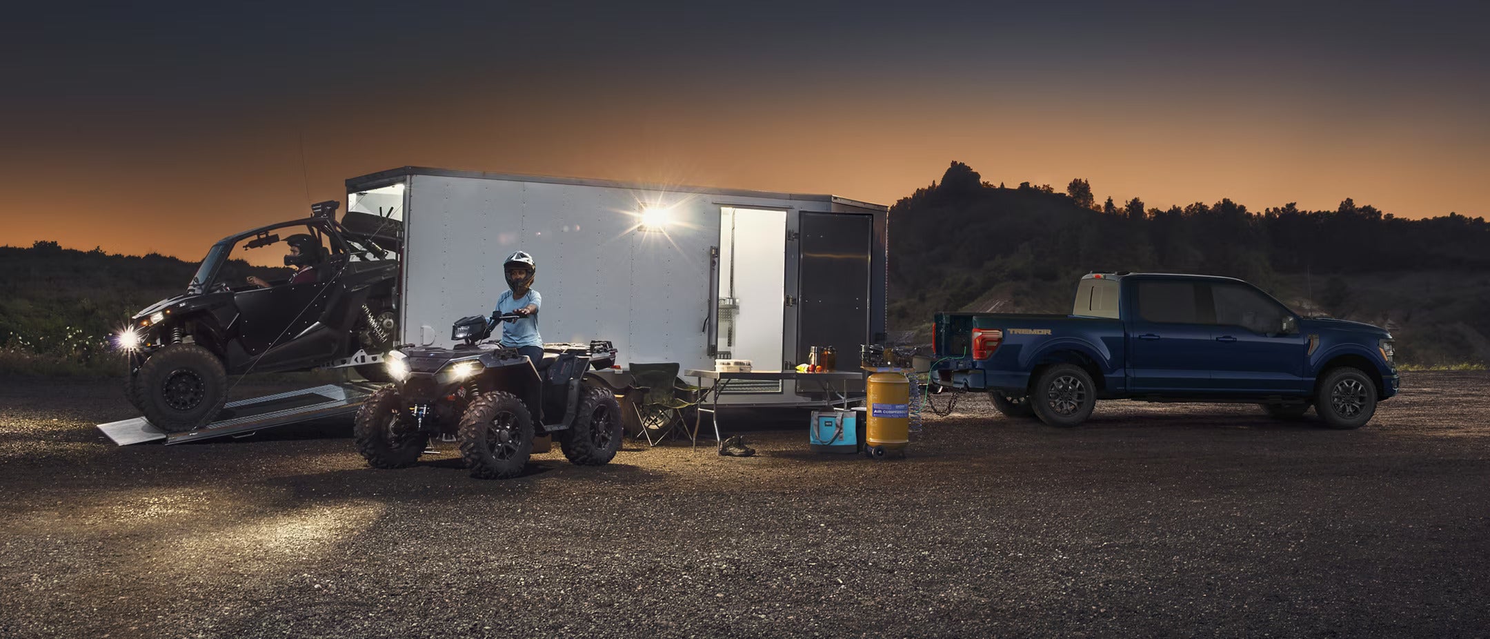 a blue ford f-150 parked at dusk with a box trailer hooked up unloading atvs