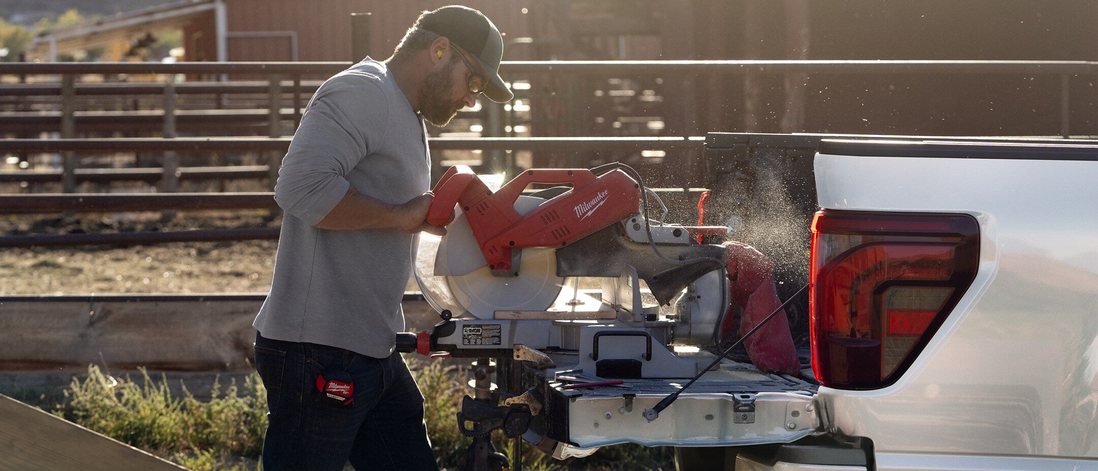 a man using a miter saw on the back of a white ford f-150 on a ranch