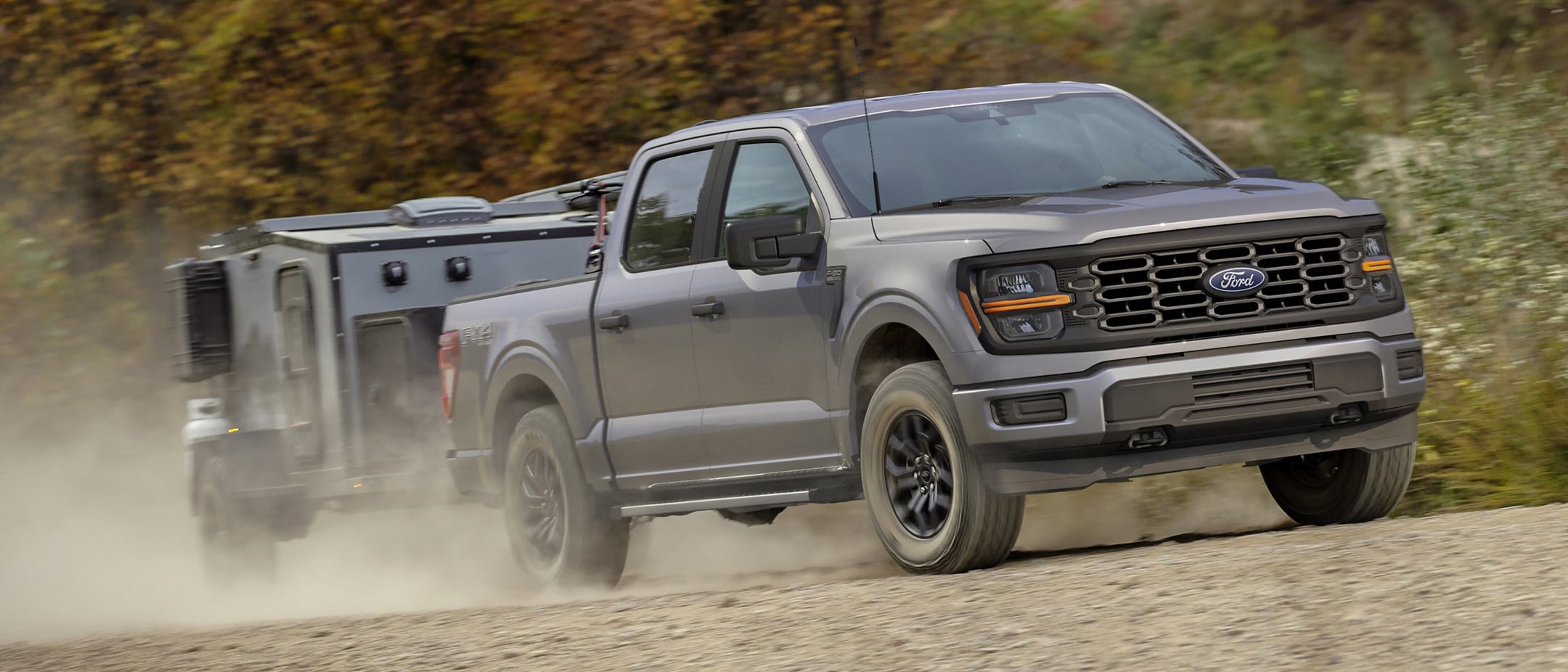 a gray ford f-150 hauling a compact camper on a dirt road
