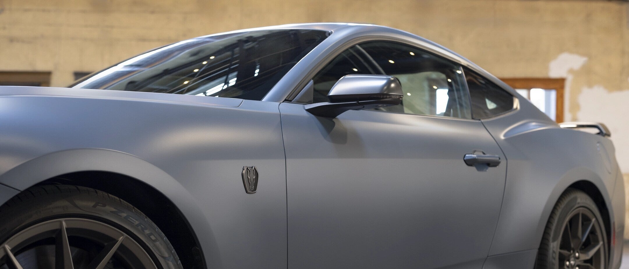 Side view of a blue 2025 Ford Mustang GT parked in a modern urban setting.