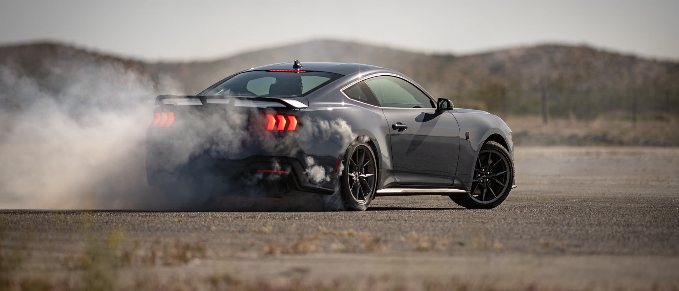 Rear-side view of a 2025 Ford Mustang performing a drift, with smoke billowing from the tires.
