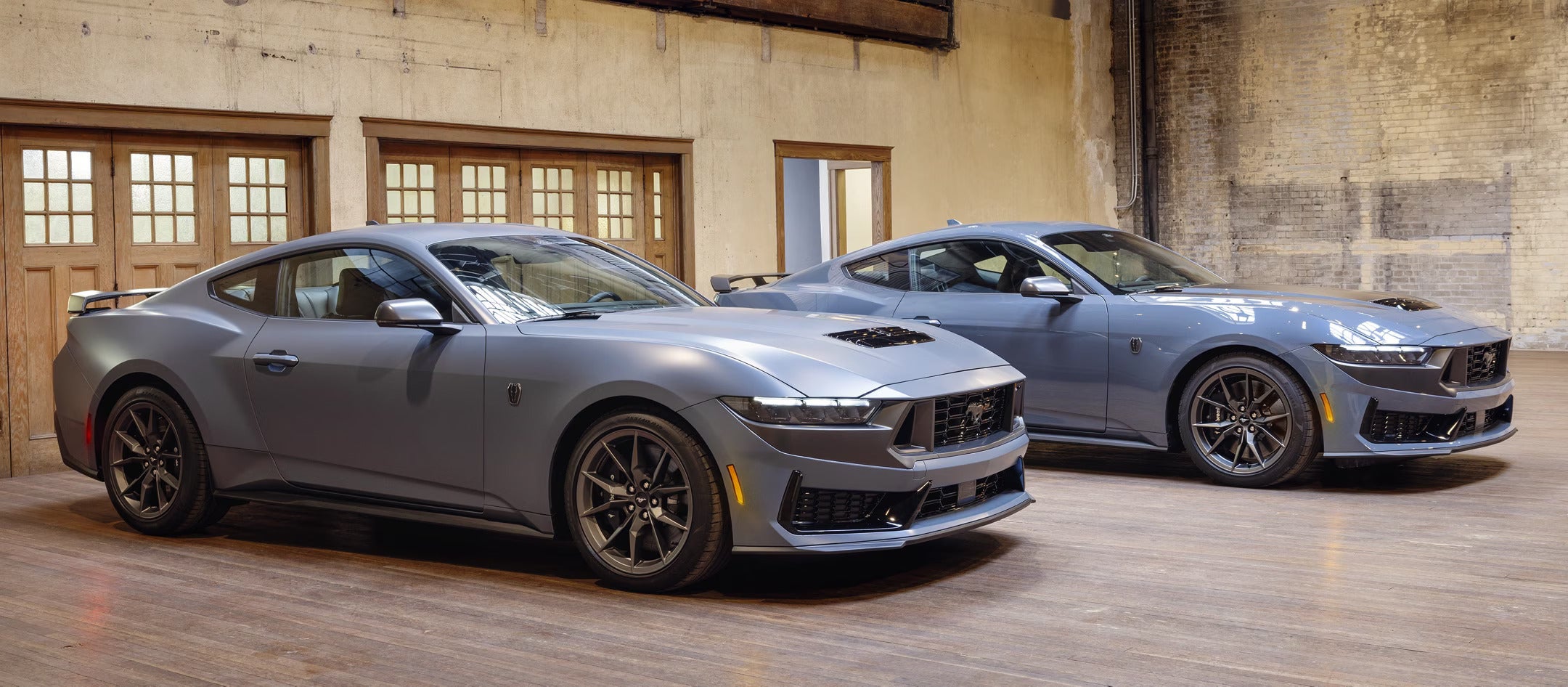 Two gray 2025 Ford Mustangs parked side by side in an indoor industrial setting