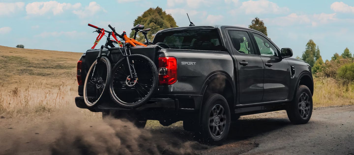 A black truck driving off-road with bikes in the bed.